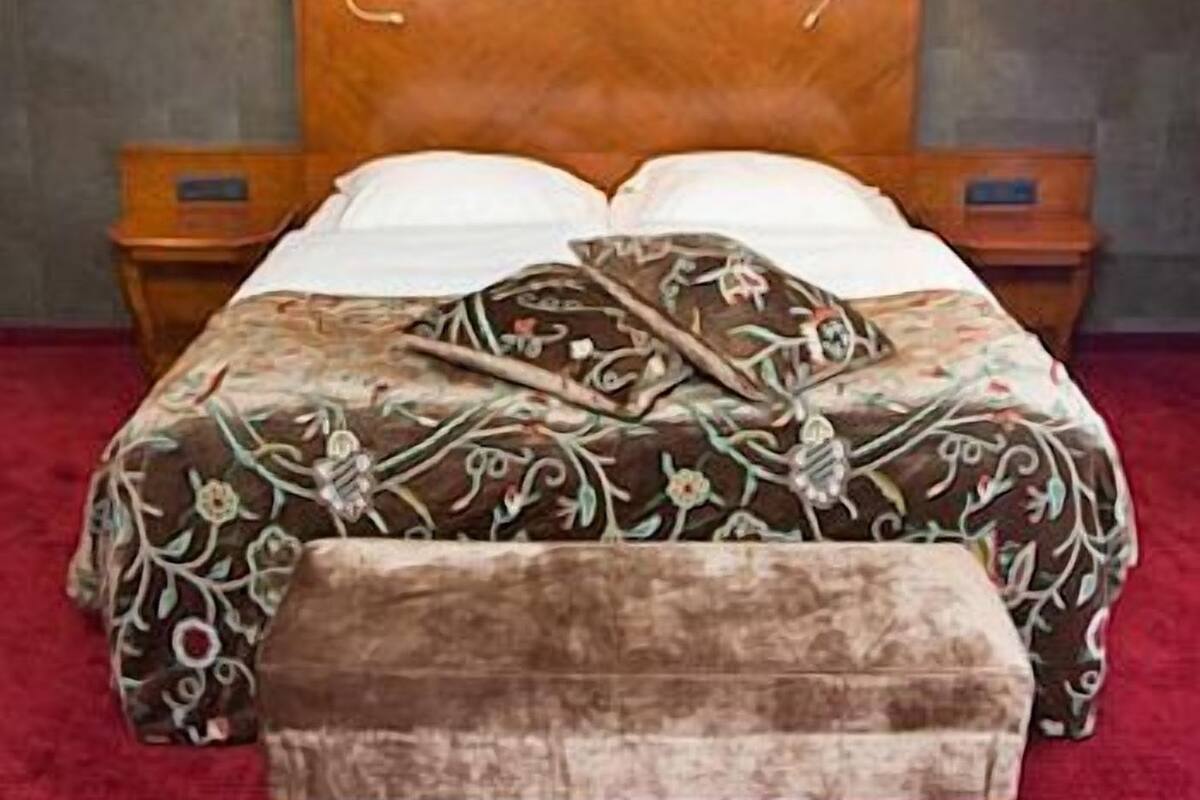 Un lit avec une tête de lit en bois, deux lampes de chevet et une couvre-lit à motifs floraux.
