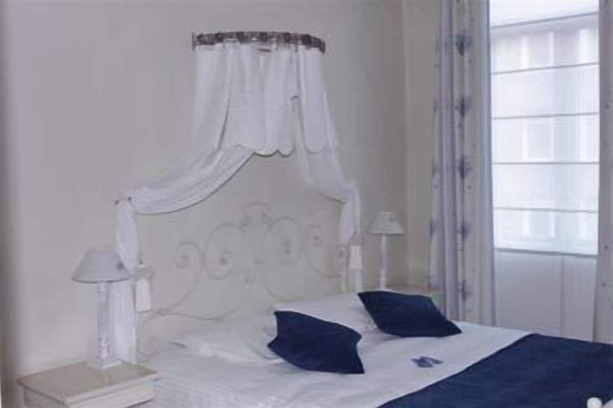 Une chambre à coucher avec un lit à baldaquin, deux tables de chevet et une fenêtre avec des stores.