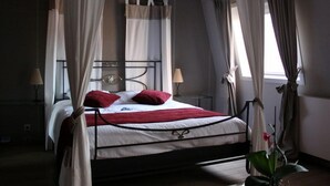 A four-poster canopy bed with a white and red bedspread, two bedside lamps, and a nightstand with a lamp.