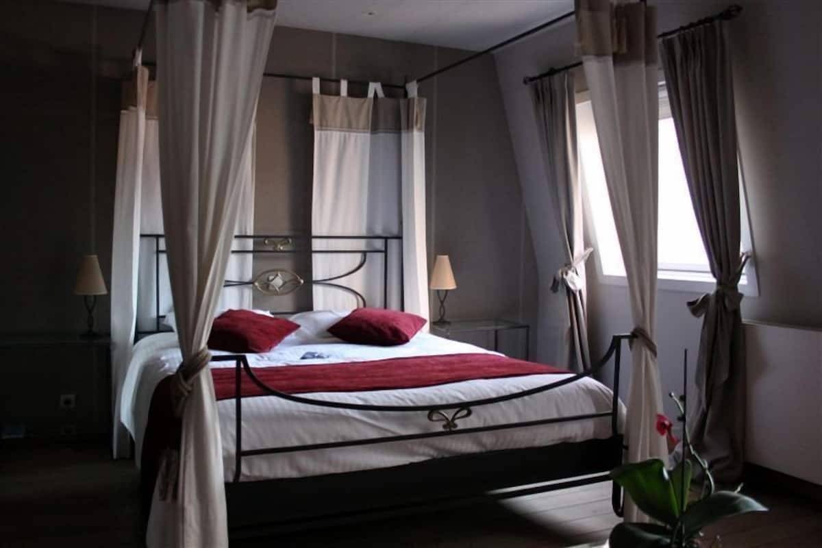 Un lit à baldaquin à quatre poteaux, avec une couvre-lit blanche et rouge, deux lampes de chevet et une table de chevet avec une lampe.