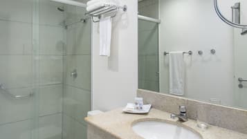 Un baño moderno con cabina de ducha de vidrio, inodoro blanco, lavabo con encimera y un espejo grande.
