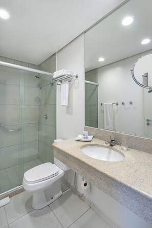 Un baño moderno con cabina de ducha de vidrio, inodoro blanco, lavabo con encimera y un espejo grande.