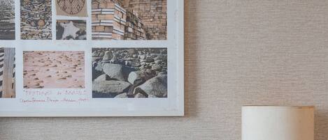 Un collage enmarcado de fotografías en una pared, una lámpara sobre una mesa y una silla.
