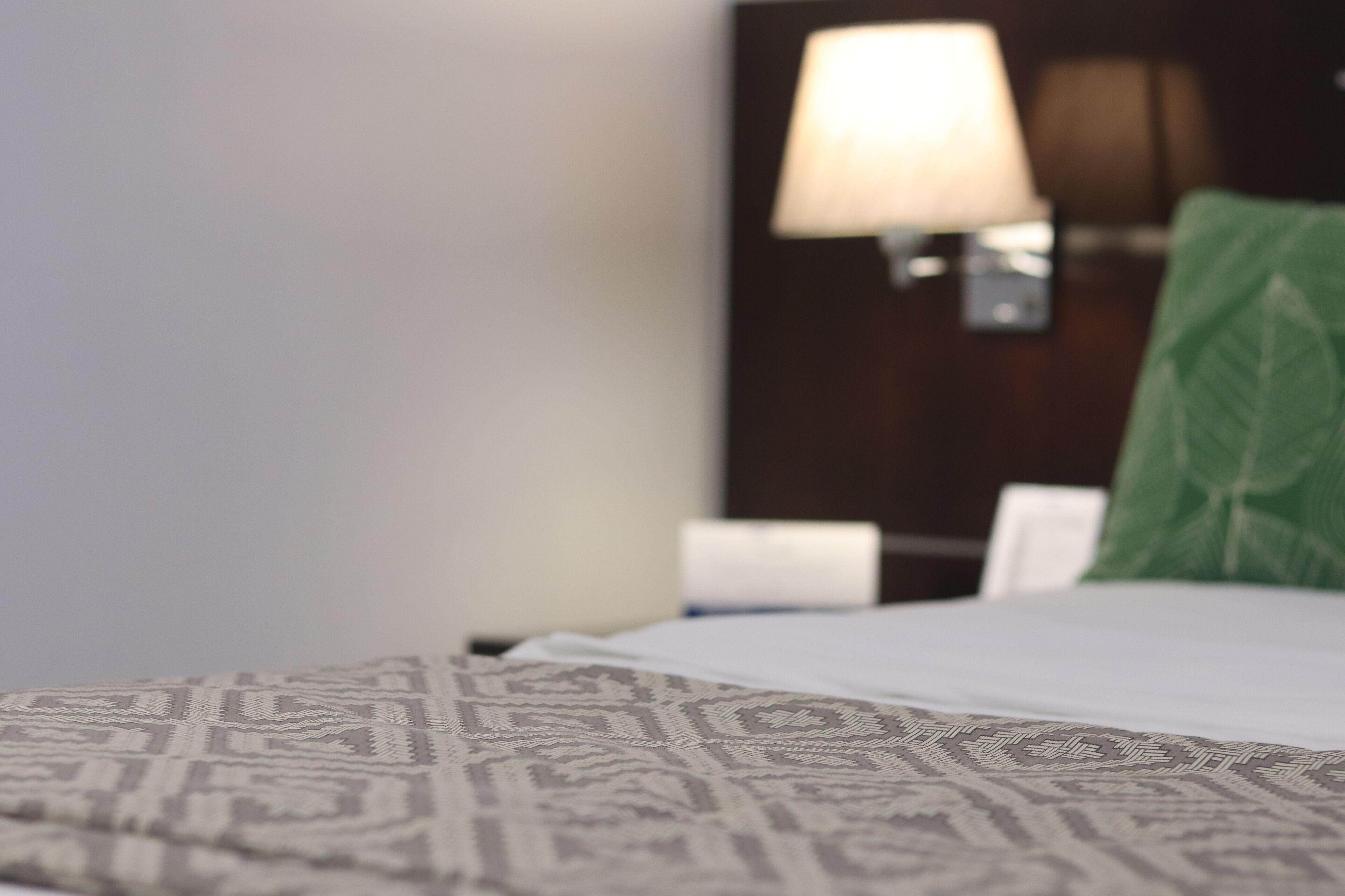 A bed with patterned bedding, a green pillow, and a wall-mounted lamp.