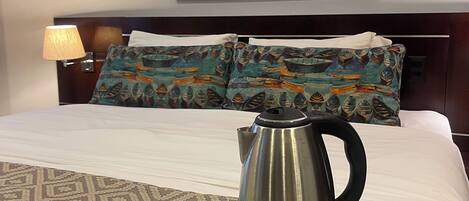A neatly made bed with a patterned bedspread, a tray with tea bags, a teapot, and a cup and saucer on a black tray.