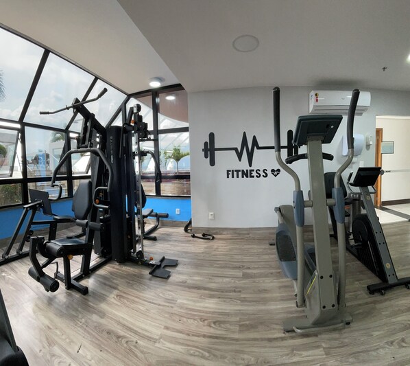 Un gimnasio con equipo de ejercicio, una pared con el texto 'FITNESS' y ventanas amplias.