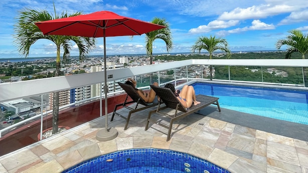 A rooftop pool area with lounge chairs and a red umbrella, overlooking a cityscape. - Manaus Hotéis - Millennium (Manaus)