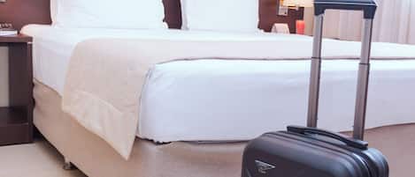 A hotel room with a bed, a nightstand, a lamp, and a suitcase.