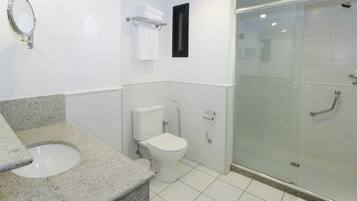 Un baño moderno con encimera de granito, inodoro, cabina de ducha de vidrio y un espejo pequeño.