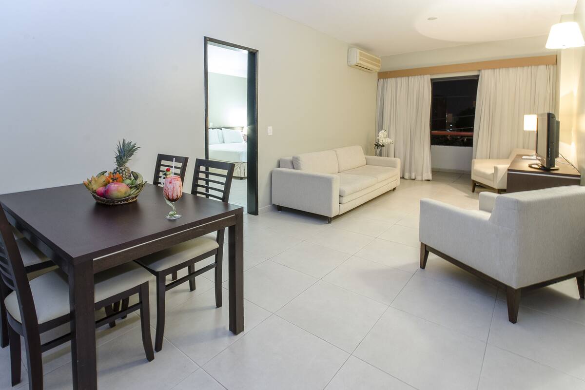 A modern hotel room with a dining area, a sofa, and a TV.