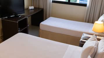 Quarto de hotel com uma cama, uma escrivaninha com televisão e uma janela com vista para a cidade.