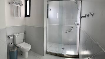 A modern bathroom with a toilet, a glass-enclosed shower, and a trash bin.