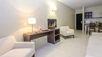 Een moderne hotelkamer met een bank, fauteuils, een bureau met lamp, een televisie en een eethoek met stoelen en een tafel.