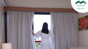 A room with a view, a white chair, a lamp, and a glass of orange juice. - Hotel Saint Paul (Manaus)