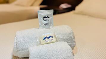 A neatly made bed with white towels and a small sachet of hand soap labeled "MANAUS HOTELS".