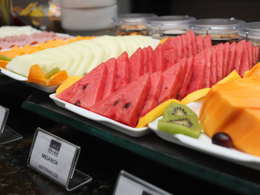 A buffet with various fruits and labeled signs for melon and watermelon.