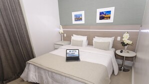 A hotel room with a bed, a bedside table with a lamp, a small round table with a vase of flowers, and two framed pictures on the wall. - Hotel Adrianópolis All Suites (Manaus)
