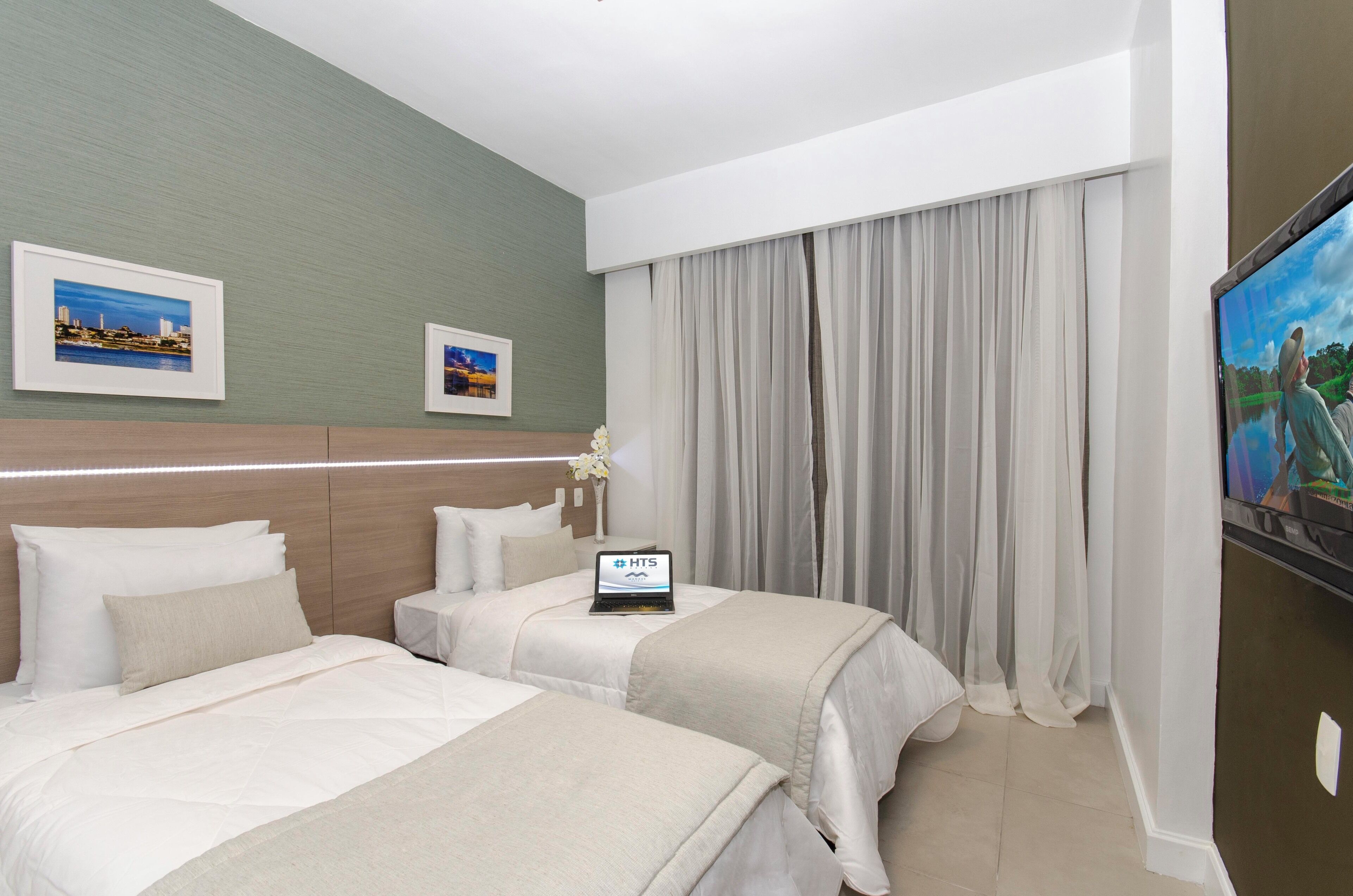 A hotel room with two beds, a flat-screen TV, a laptop, and framed pictures on the wall.