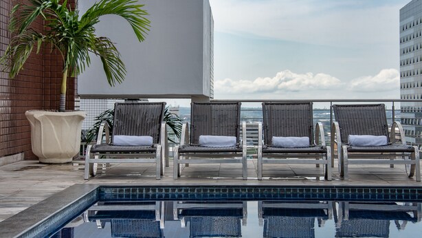 A rooftop pool area with lounge chairs and a palm tree. - Hotel Adrianópolis All Suites (Manaus)