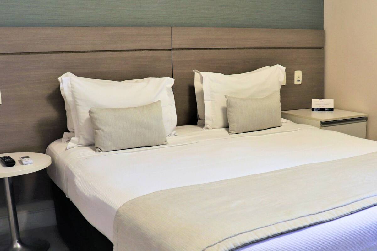 Camera d'albergo con un letto grande, due cuscini, un comodino con un telecomando e un tavolino rotondo.