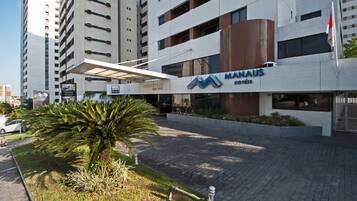 A modern hotel with a prominent 'MANHAUS' sign, a covered entrance, and a landscaped area with palm trees.