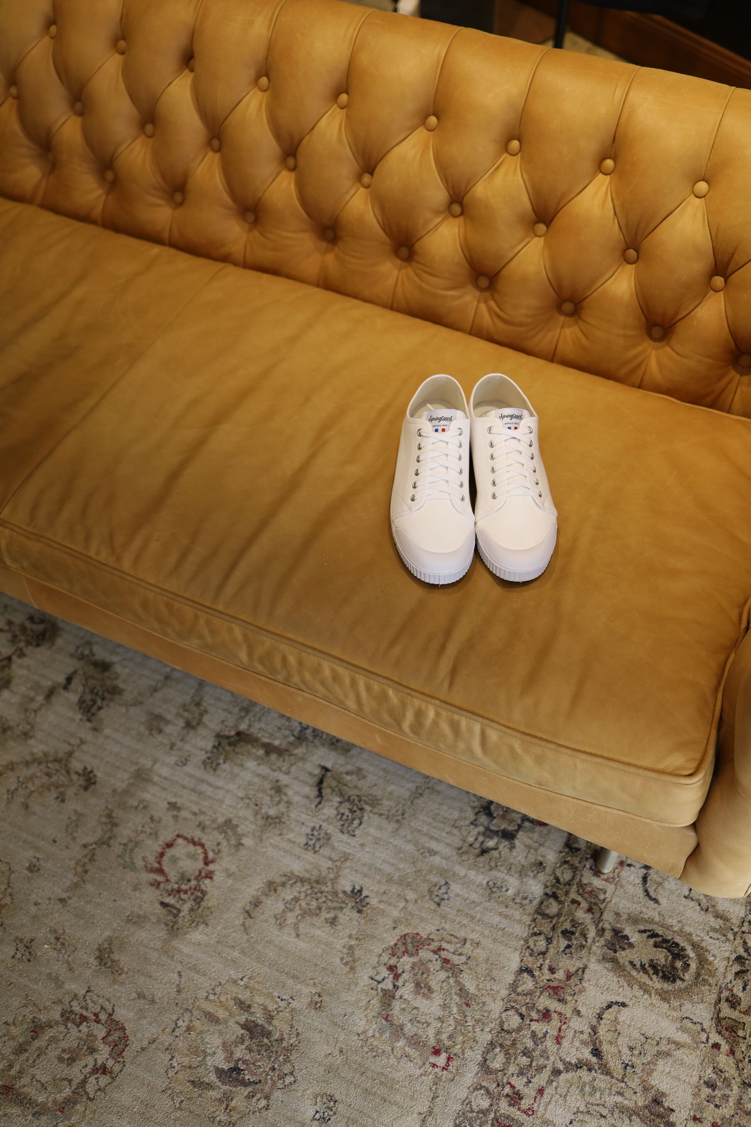 En stykke tæppebemmet sofa med et par hvide sneakers ovenpå.