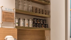 A kitchenette with a coffee maker, toaster, and shelves with jars and containers.
