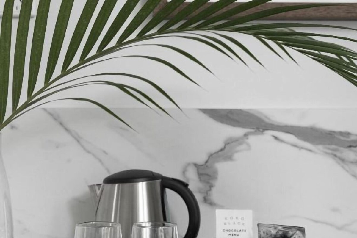 A marble wall with a black kettle and three glasses on a surface.