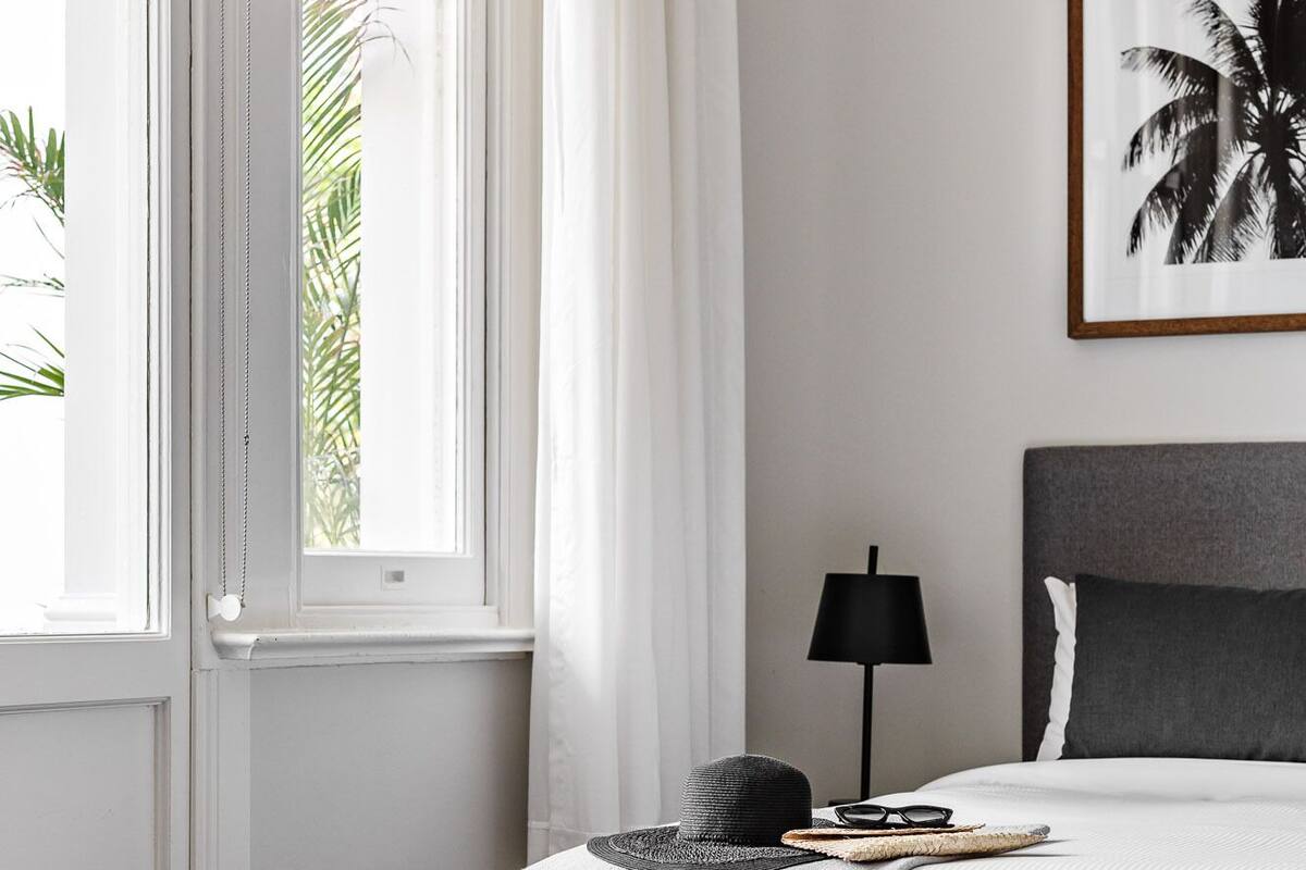 Une chambre à coucher bien rangée, avec un lit, une table de chevet, une lampe et un tableau encadré au mur.