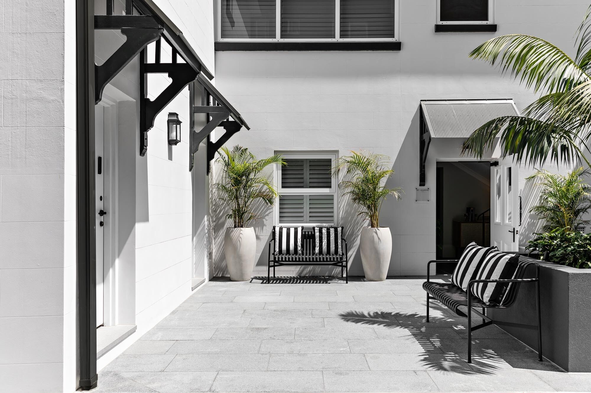 A narrow courtyard with a bench, two potted plants, and a door leading to a building.