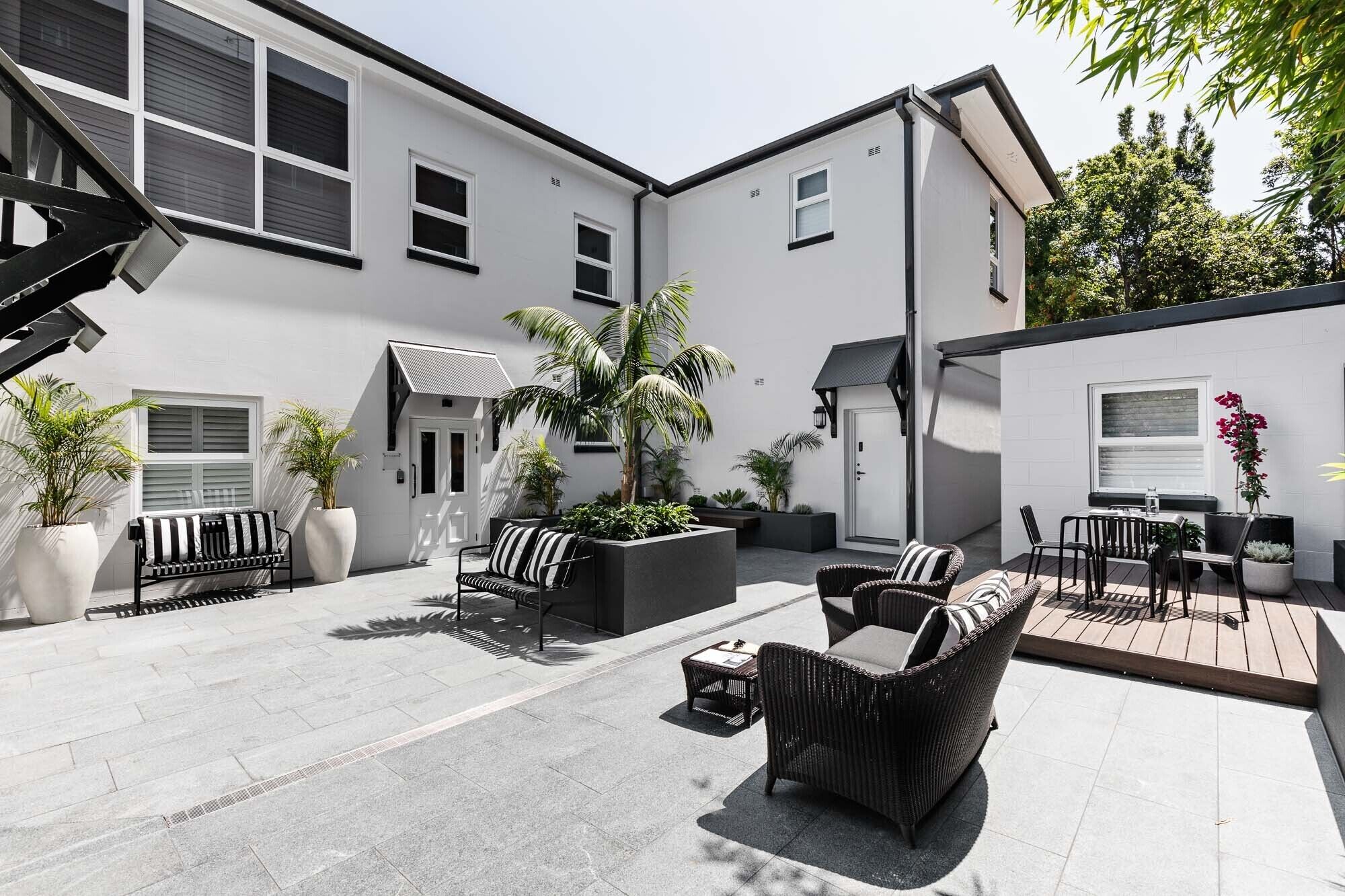 A modern outdoor patio with a black and white striped sofa, a dining table with chairs, and potted plants.