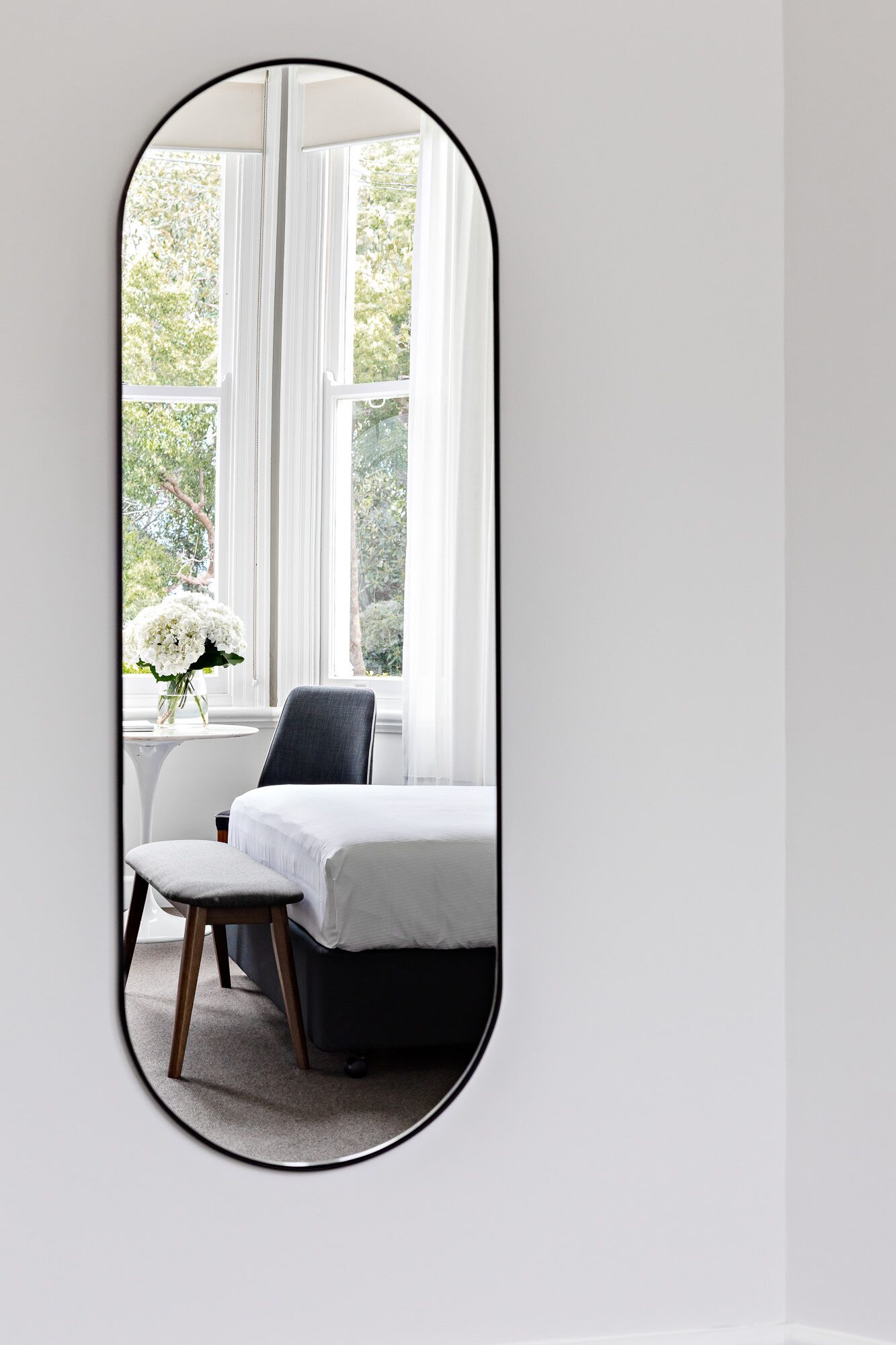 Un dormitorio con una cama, una silla y una mesa con un jarrón de flores.