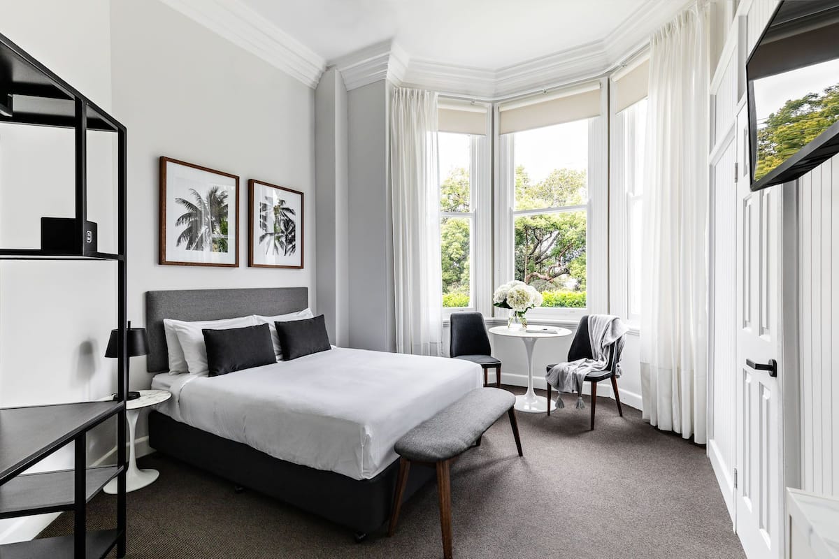 Une chambre d’hôtel moderne, dotée d’un grand lit, d’un bureau et offrant une vue sur la verdure par les fenêtres.