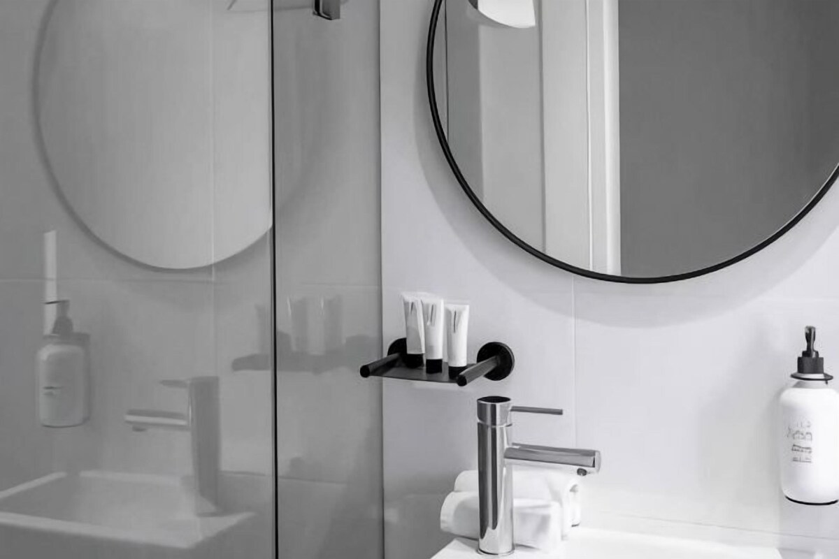 A modern bathroom with a glass shower enclosure, a round mirror, and a white sink.