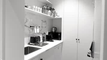 Una cocina moderna con armarios blancos, salpicadero de mármol y cafetera.
