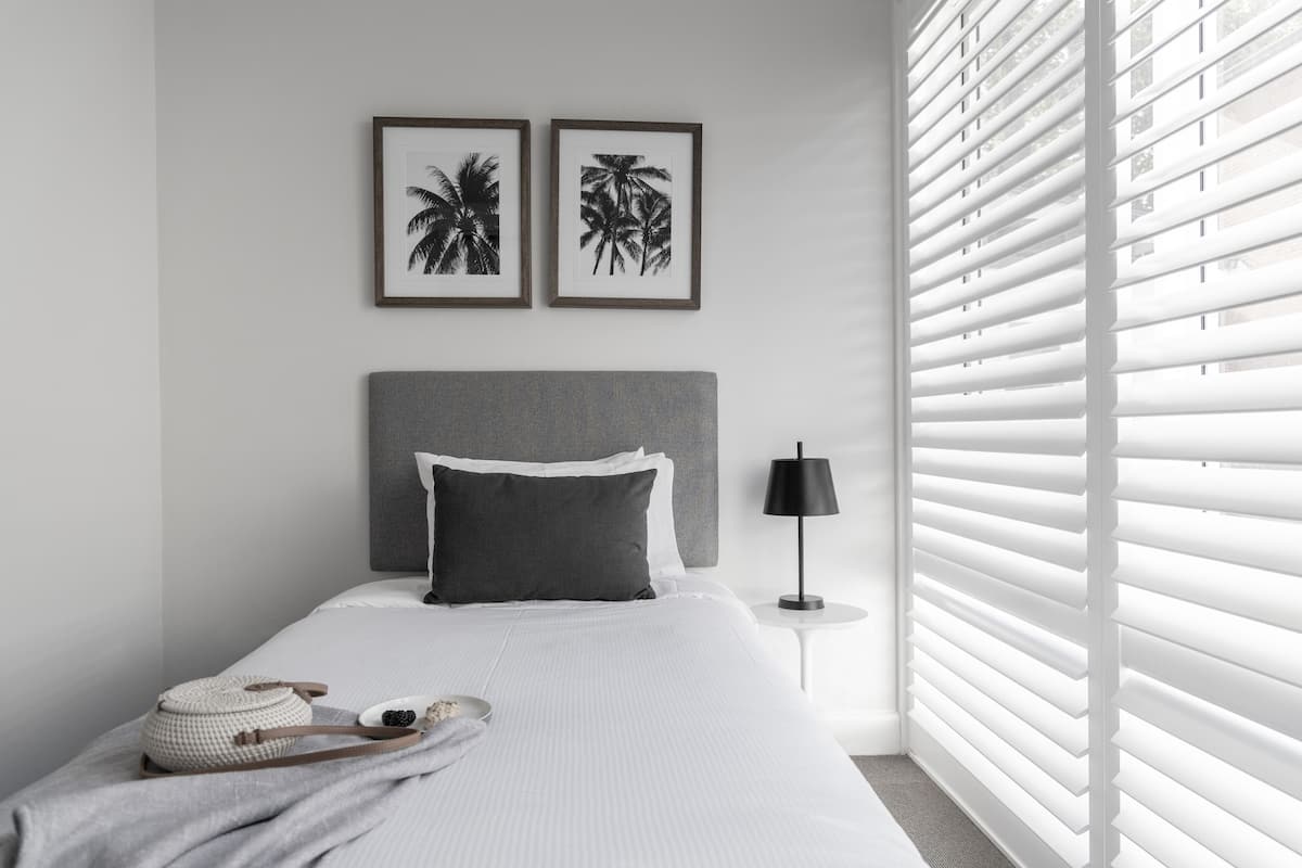 Une chambre à coucher bien rangée, avec un lit, des oreillers, une lampe de chevet et un cadre photo fixé au mur.