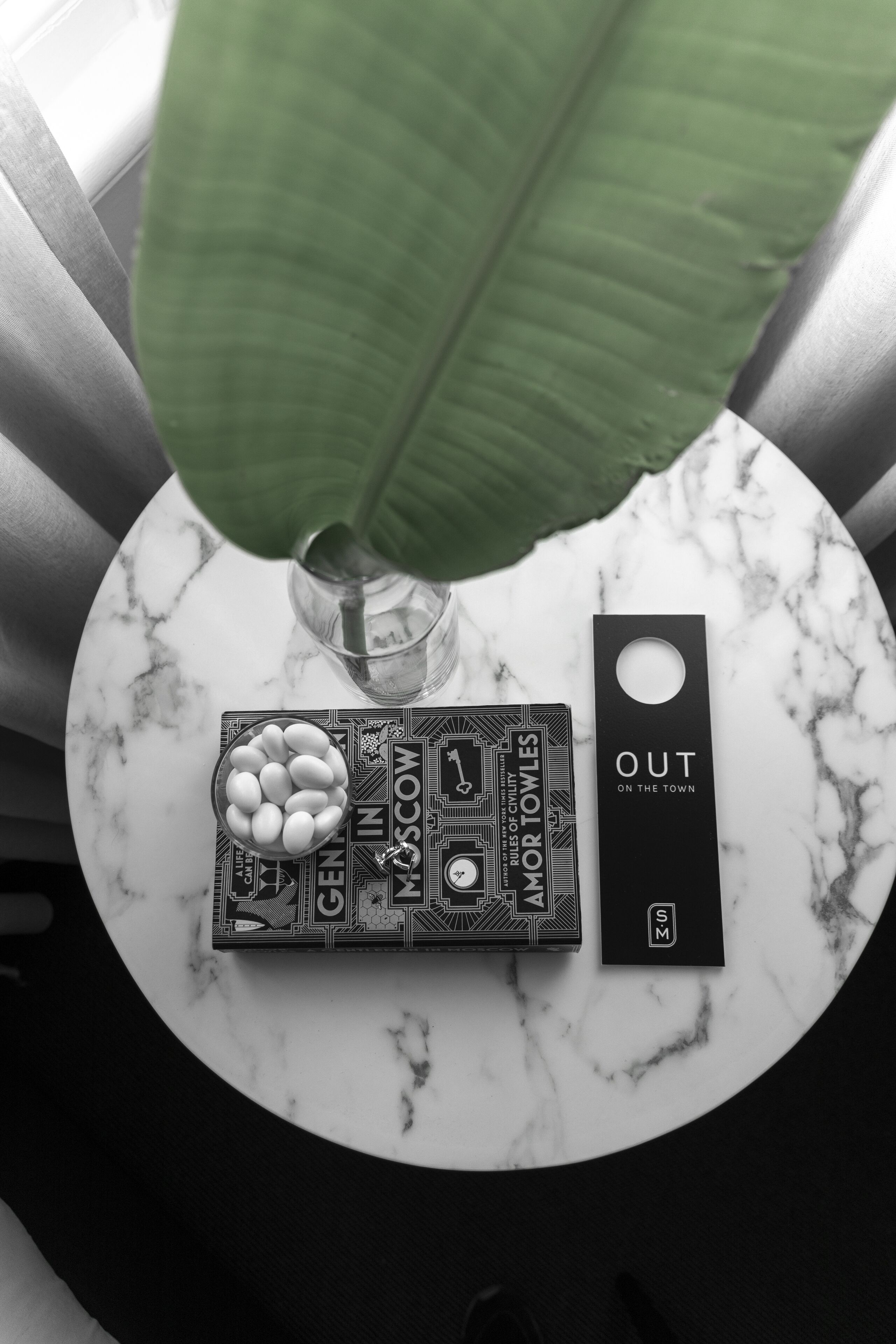 A marble table with a black and white board game, a glass vase with a green plant, and a black tag.