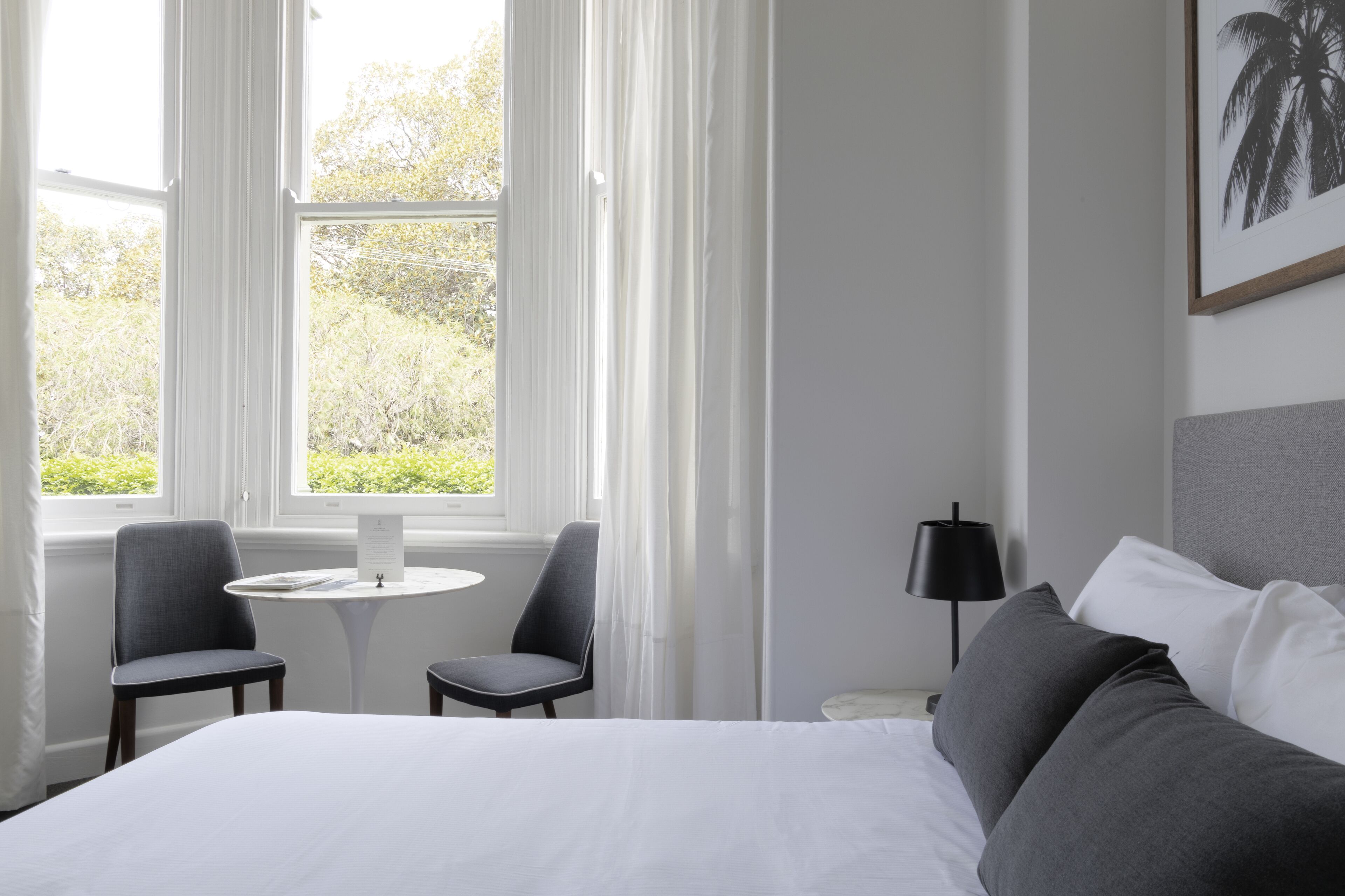 A hotel room with a large bed, two chairs, a small table, a lamp, and a window with curtains.