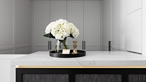 Una encimera de mármol con un florero de flores blancas, una tarjeta pequeña y un adorno con forma de piña.
