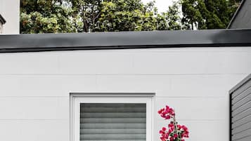 Une terrasse avec une table et des chaises, un pot de fleurs et une fenêtre avec des stores.