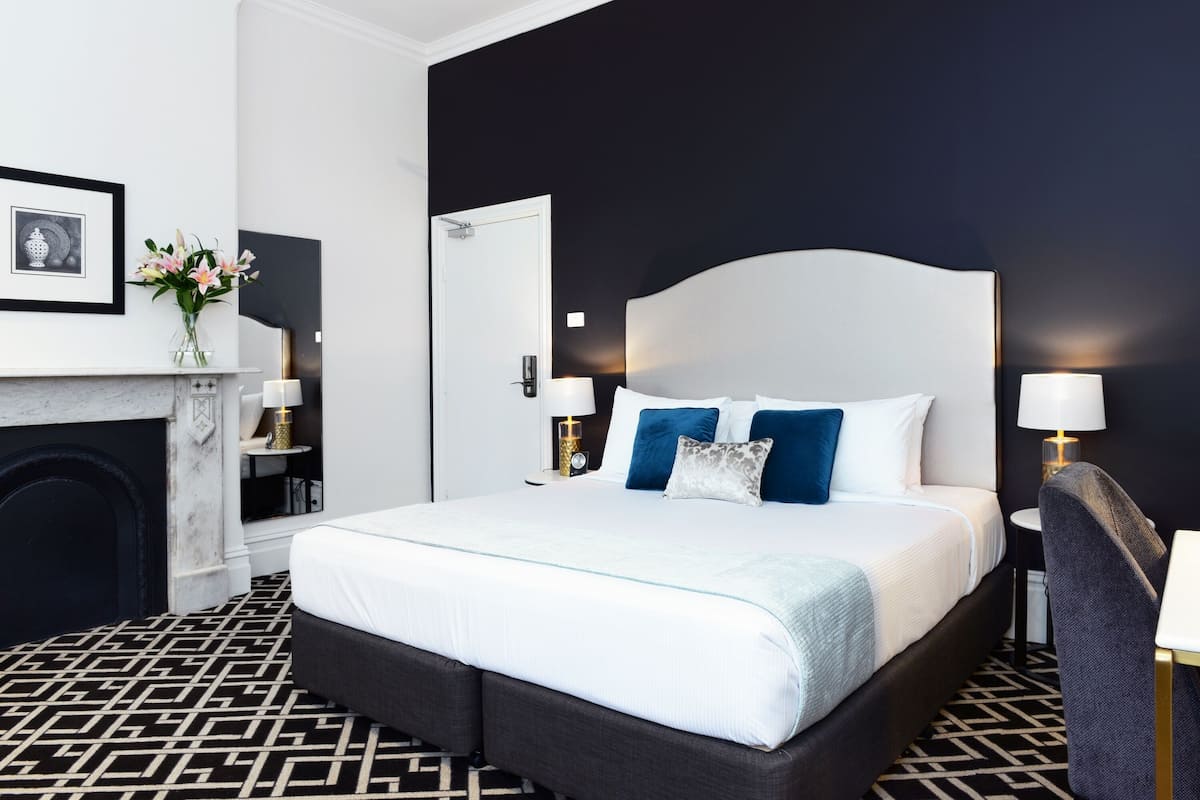 A modern hotel room with a large bed, a fireplace, and a black and white patterned floor.
