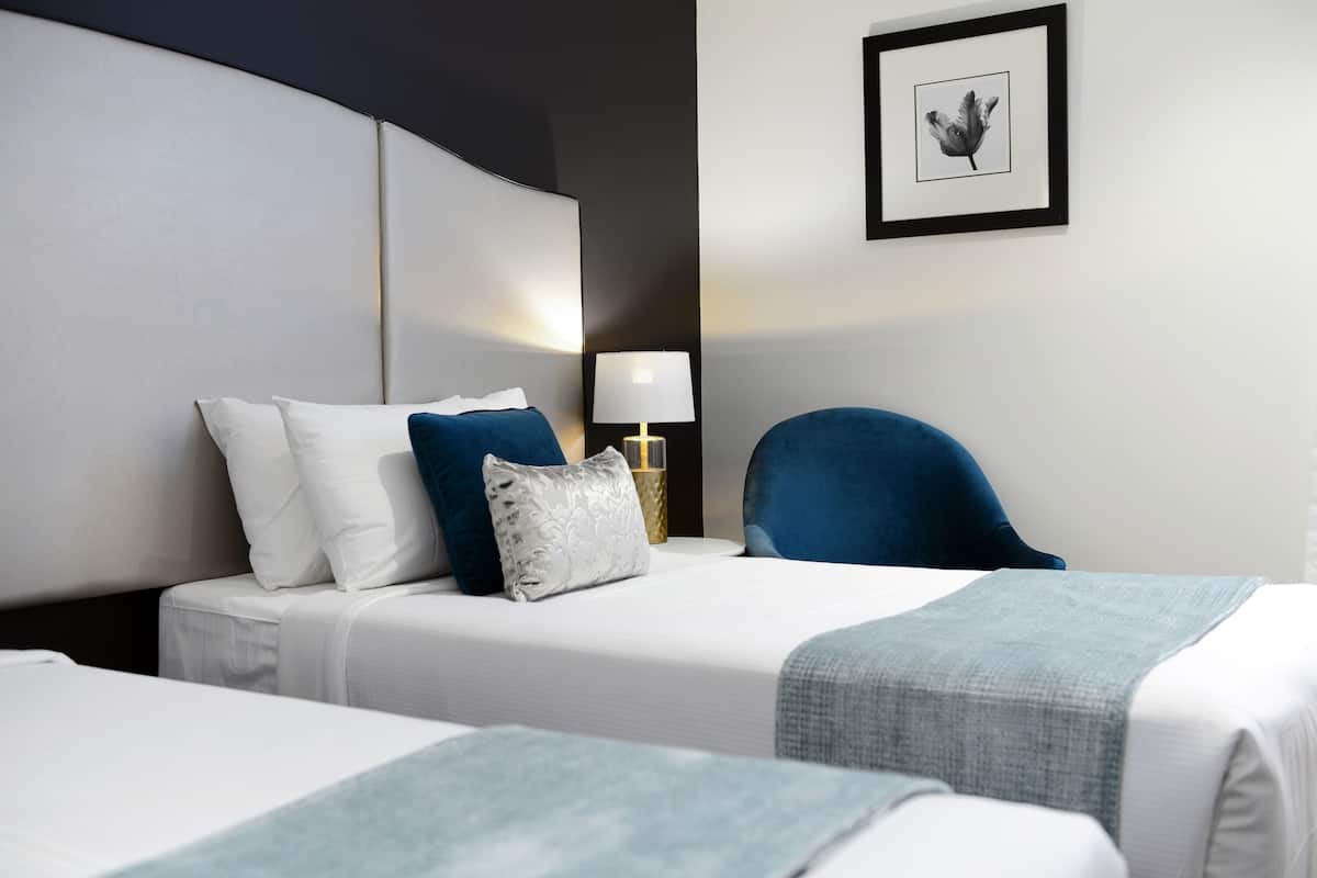 A hotel room with two beds, a nightstand, a lamp, and a framed picture on the wall.