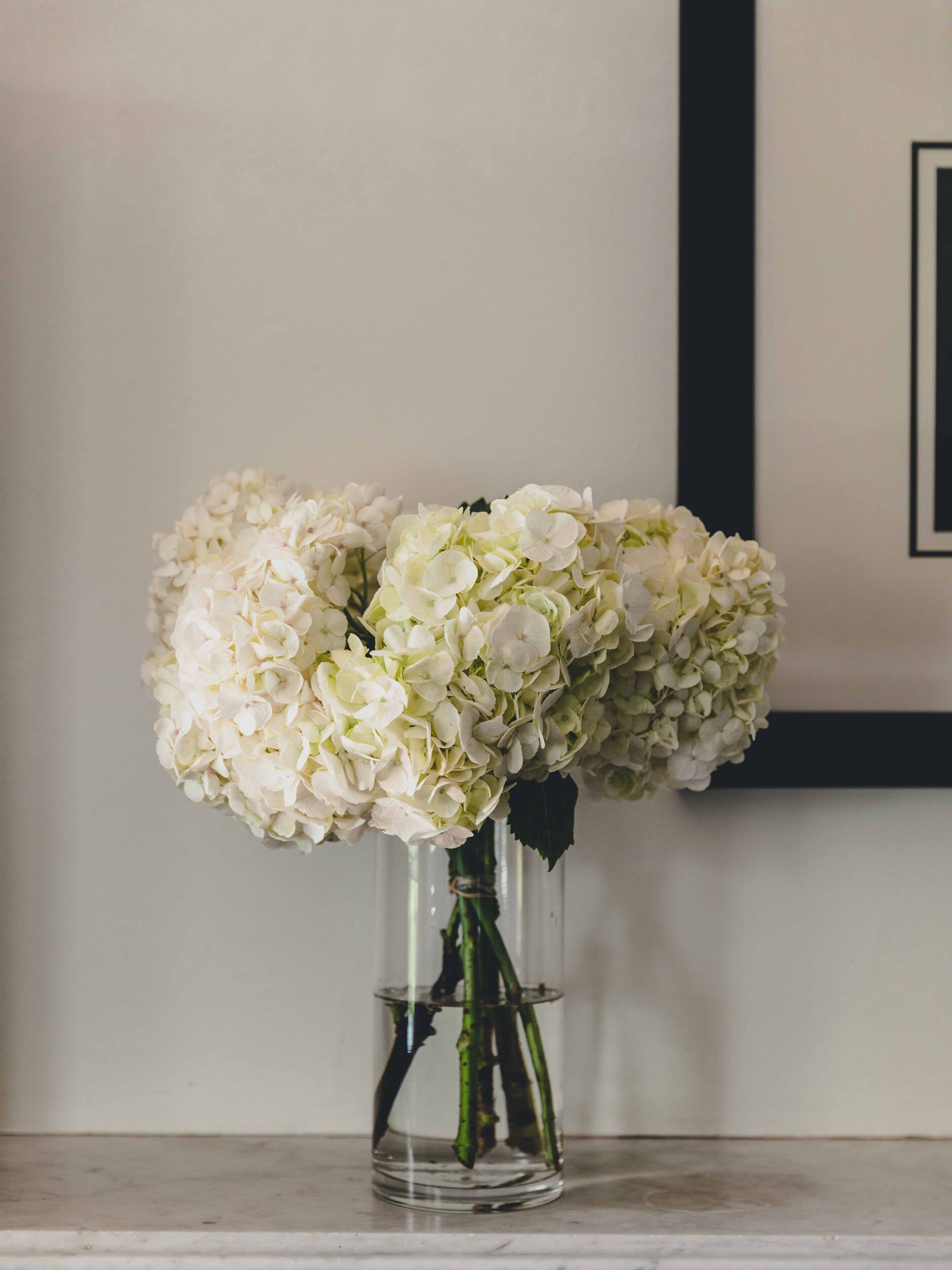 A clear glass vase with white flowers on a marble surface.