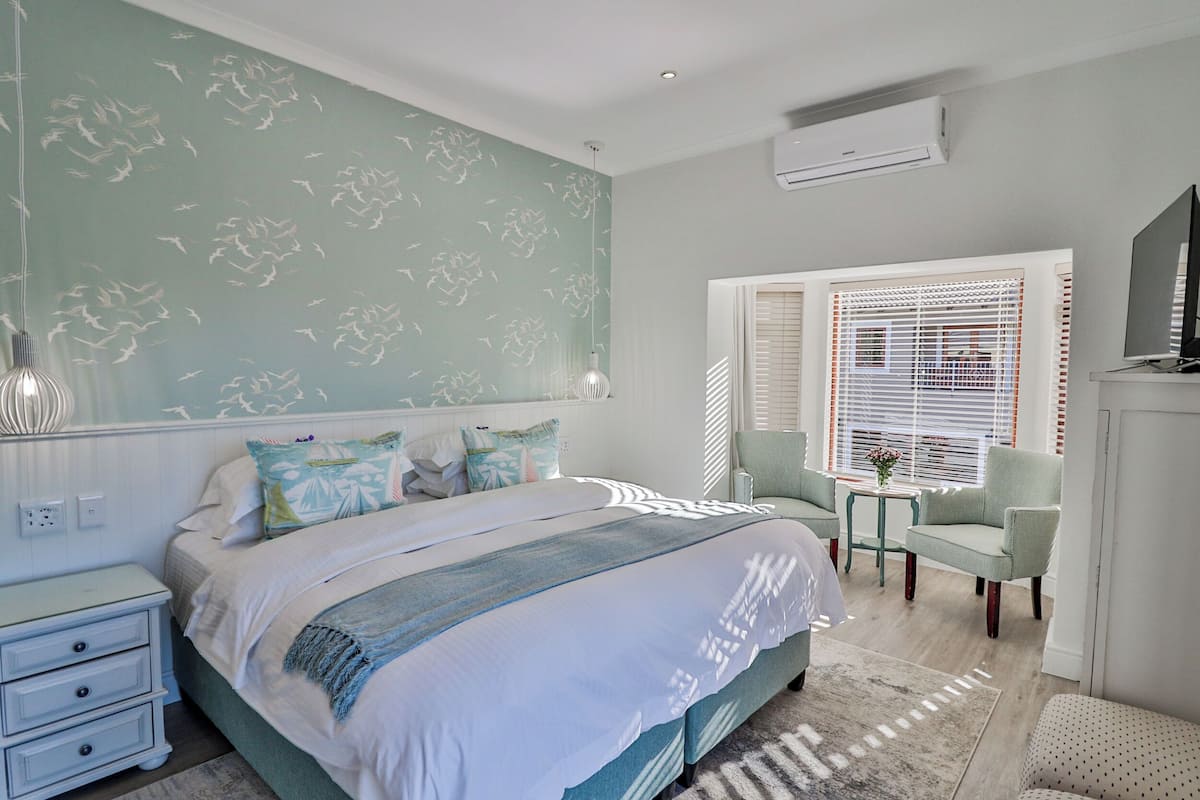 Une chambre à coucher comprenant un lit, des tables de chevet, une chaise, une petite table avec un vase et un téléviseur.