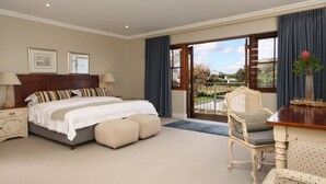 A bedroom with a large bed, a chair, a table, and a view of the outdoors through a glass door. - Lavender Manor Guest Lodge (Hermanus)