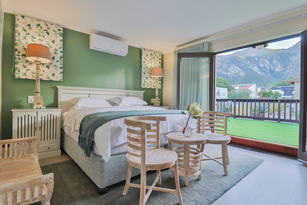 Une chambre d’hôtel avec un lit, deux chaises, une petite table et une vue sur les montagnes depuis un balcon.
