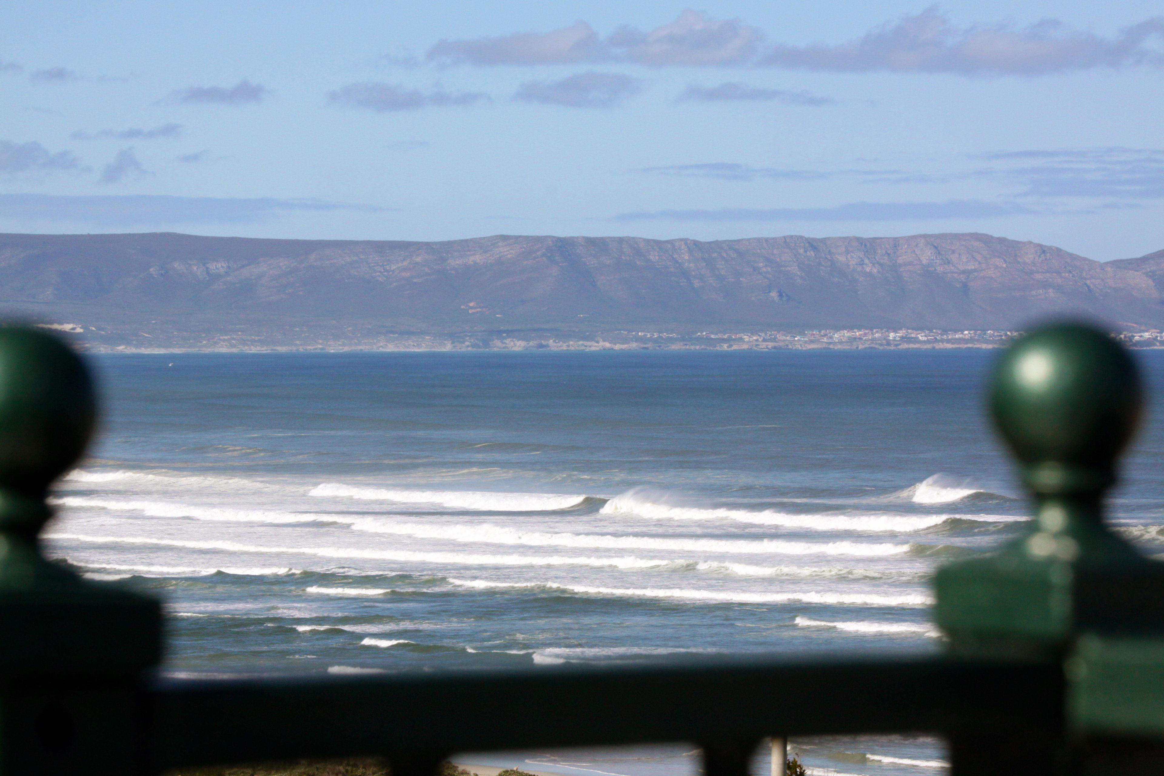 A coastal view with waves, a distant town, and mountains.