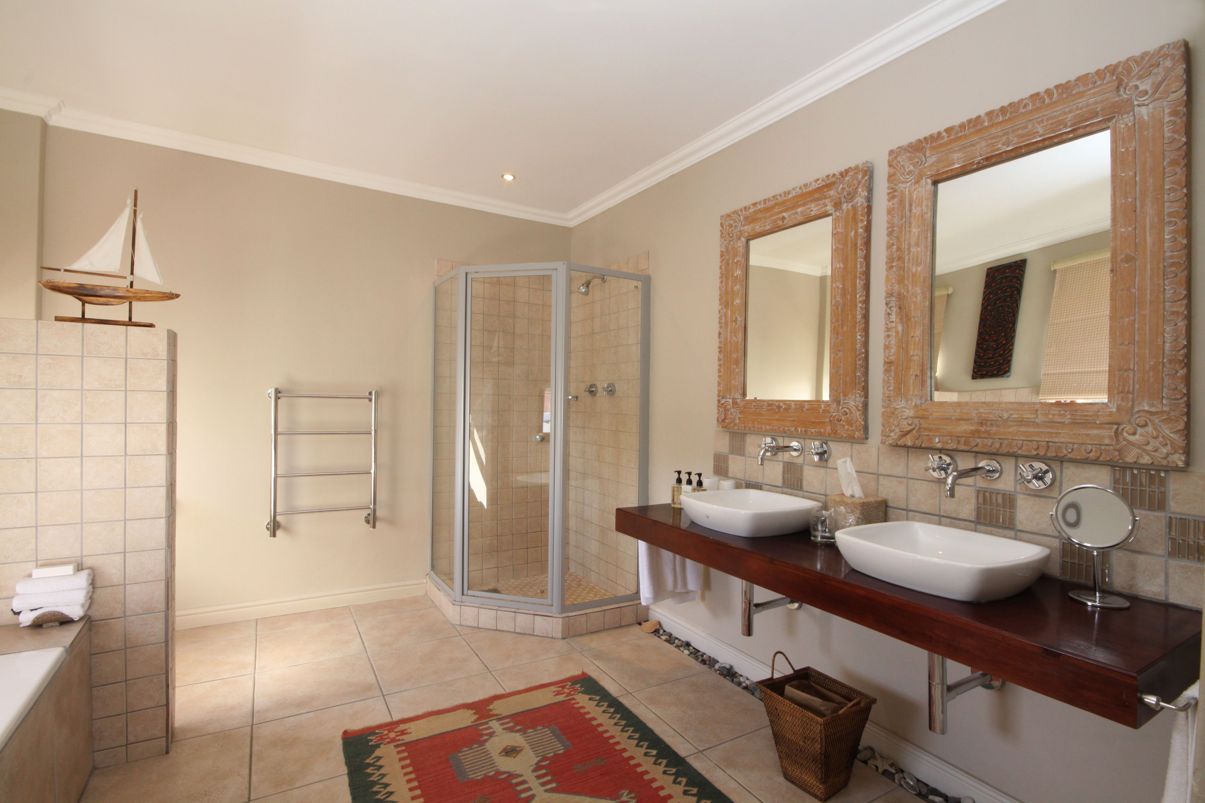 Un baño con ducha de vidrio, dos lavamanos y espejos decorativos.
