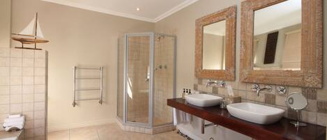 Un baño con ducha de vidrio, dos lavamanos y espejos decorativos.