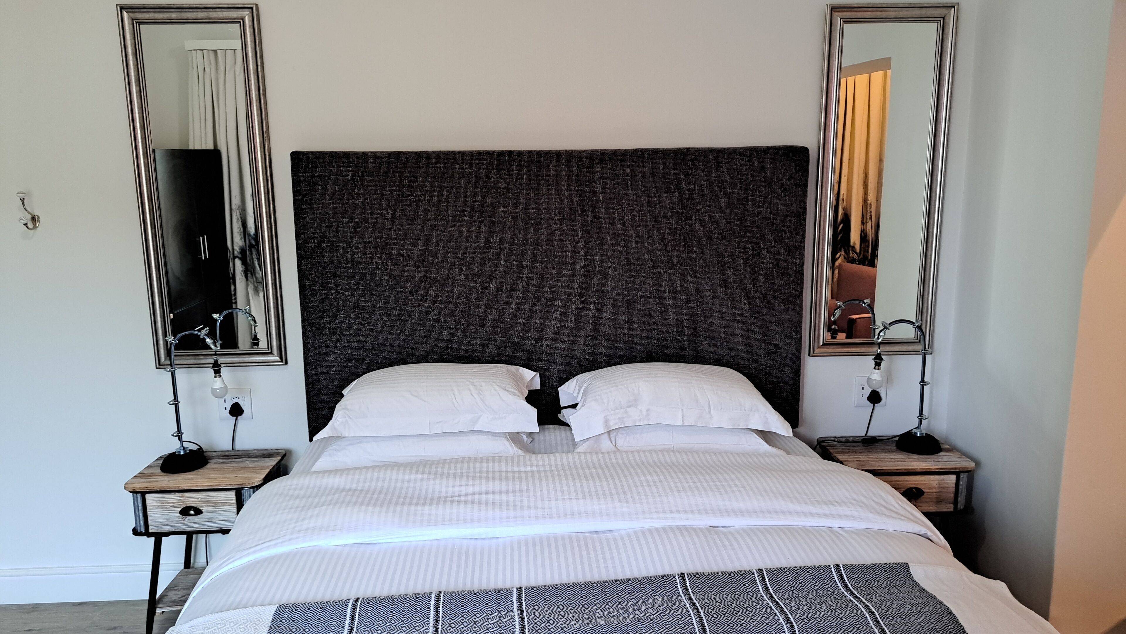 A double bed with a dark headboard, two bedside tables with lamps, and two wall-mounted mirrors.